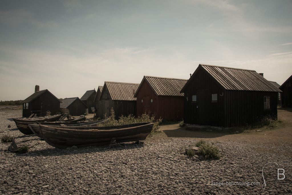 Ein altes schwedisches Fischerdorf auf Farö. Im Vordergrund liegen alte Fischerboote an Land. Dahinter stehen viele kleine Fischerhütten.