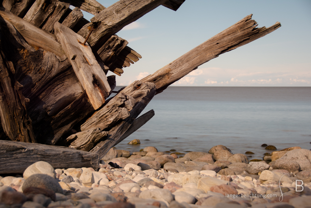 Vor langer Zeit ist auf einer schwedischen Insel ein Segelschiff auf Grund gelaufen. Das Wrack sieht man im Vordergrund während im Hintergrund die Spiegelglatte Ostsee zu erkennen ist.